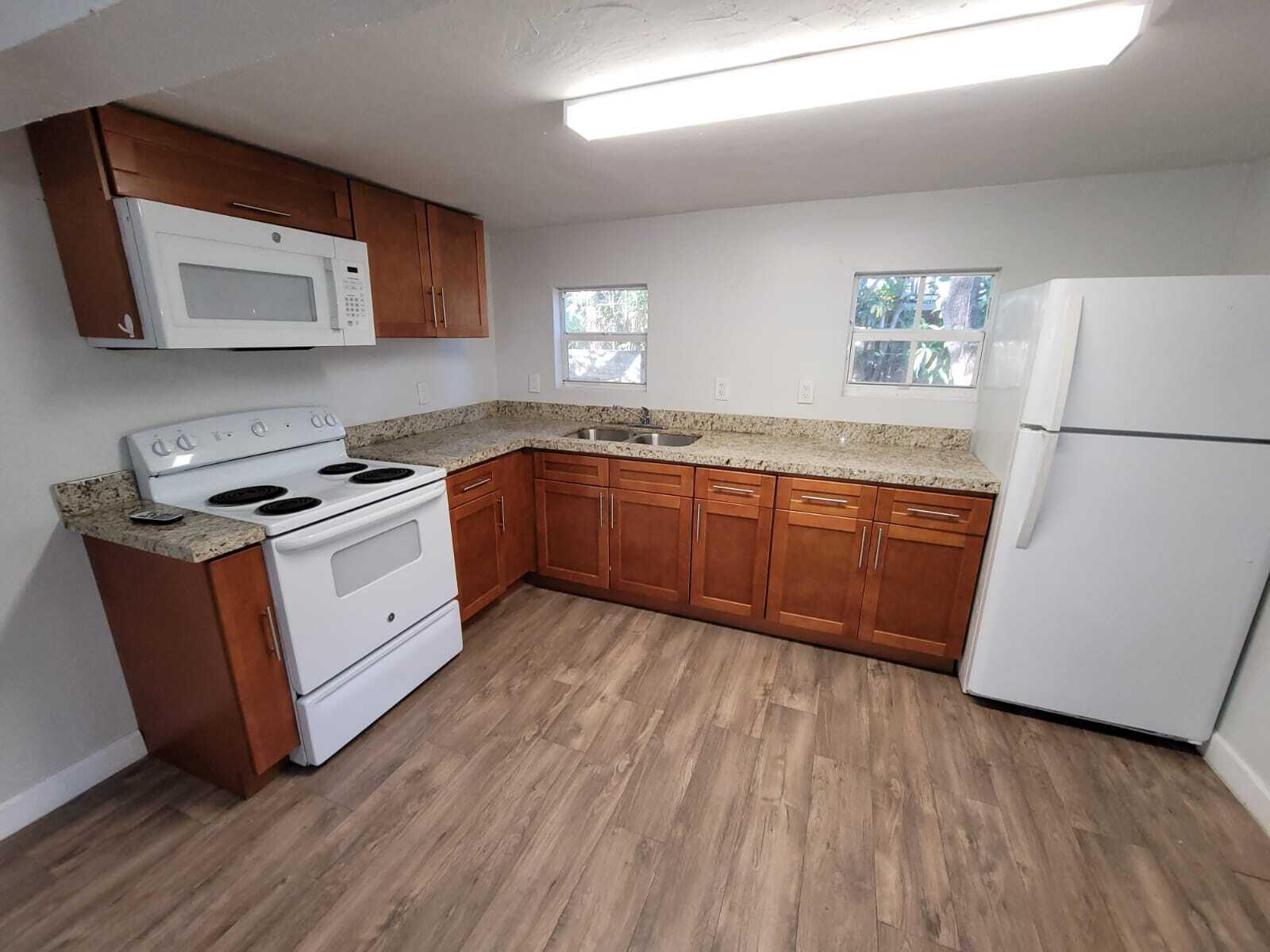 A kitchen features wood cabinets, granite countertops, white appliances, and light wood-look flooring — 210 SW 7th Street, Dania Beach FL 33004, DANIA BEACH, FL