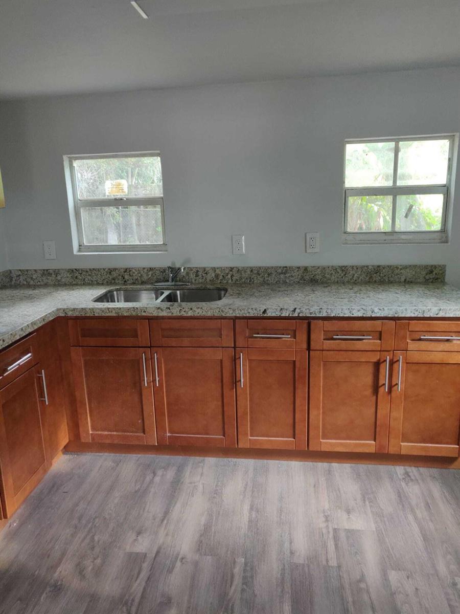 A kitchen features wood cabinets, granite countertops, a stainless steel sink, and two windows — 210 SW 7th Street, Dania Beach FL 33004, DANIA BEACH, FL