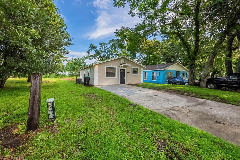 A tan single-story house with a concrete driveway sits on a grassy lot with trees — 523 CARVER BOULEVARD, ORLANDO, FL
