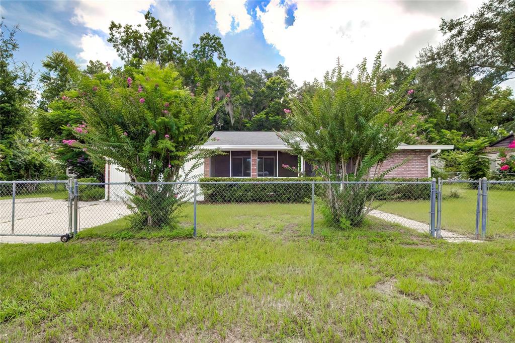 A single-story house with a screened porch and brick accents sits behind a chain-link fence — 614 POWELL STREET, WILDWOOD, FL