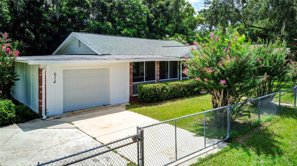 A single-story house with a white garage, a screened porch, and a chain-link fence — 614 POWELL STREET, WILDWOOD, FL
