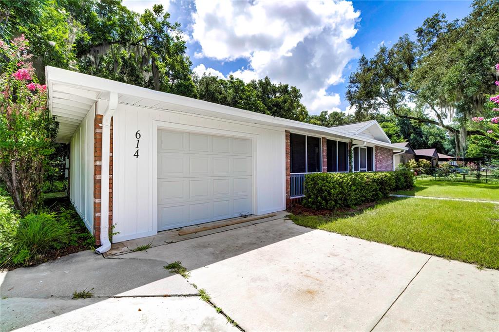 A white house exterior features a single-car garage, a screened porch, and a concrete driveway — 614 POWELL STREET, WILDWOOD, FL