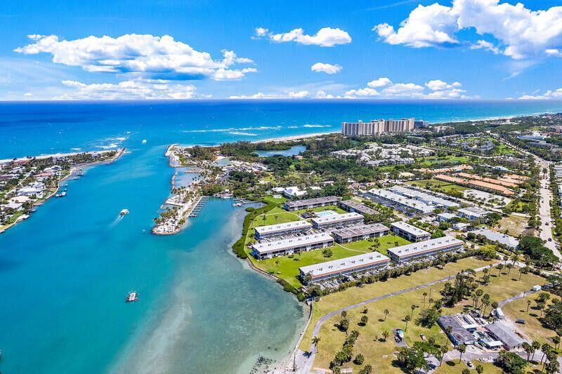 An aerial view shows a coastal inlet with multi-story apartment buildings and surrounding green space — 300 Ocean Trail Way # 1008, Jupiter FL 33477, JUPITER, FL