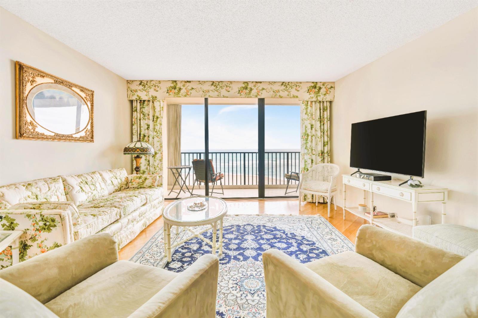 A living room features floral furniture, a blue patterned rug, and a balcony overlooking the ocean — 300 Ocean Trail Way # 1008, Jupiter FL 33477, JUPITER, FL