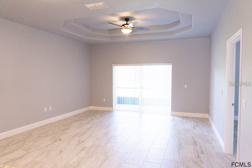 A spacious room with light tile flooring, a tray ceiling with a fan, and sliding doors — 59 FANSHAWE LANE UNIT B, PALM COAST, FL