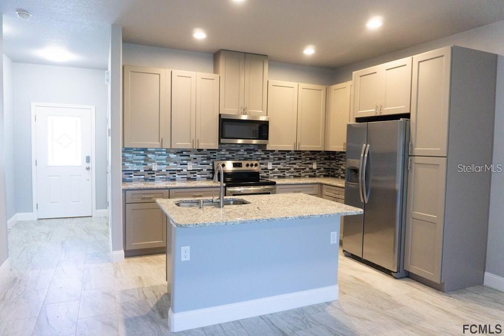 A kitchen features light gray cabinets, granite countertops, a central island, and stainless steel appliances — 59 FANSHAWE LANE UNIT B, PALM COAST, FL
