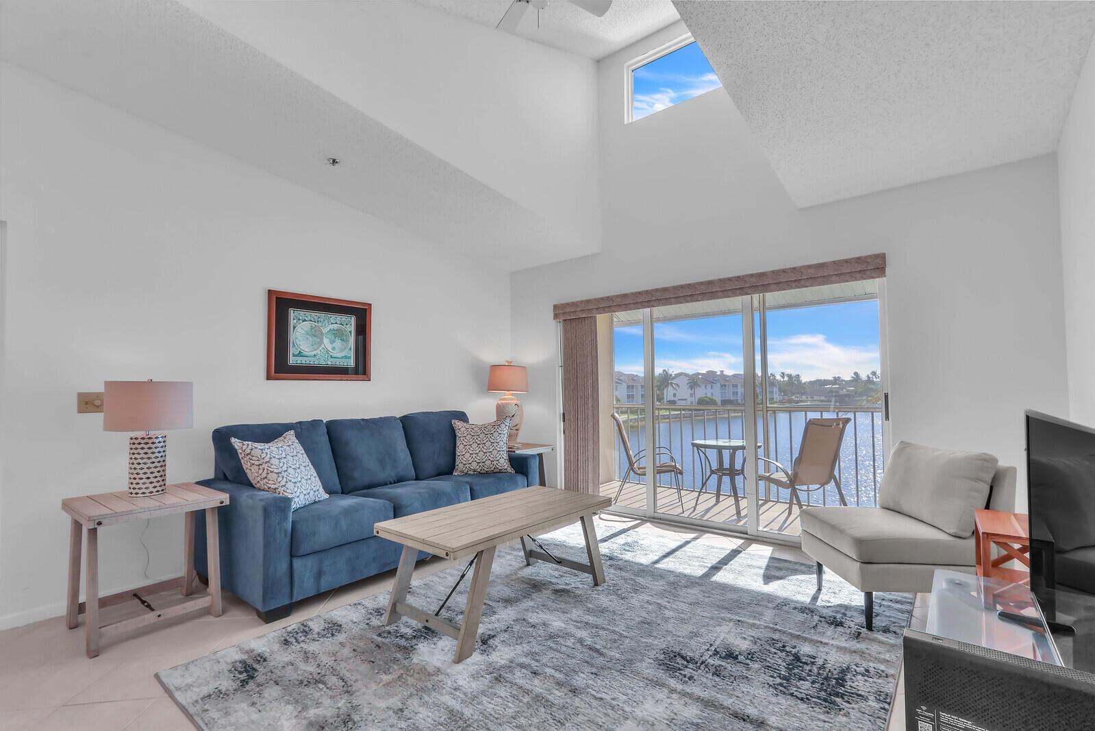 A living room with a blue sofa, coffee table, and sliding doors overlooking a lake — 4468 NE Ocean Boulevard # 3, Jensen Beach FL 34957, JENSEN BEACH, FL