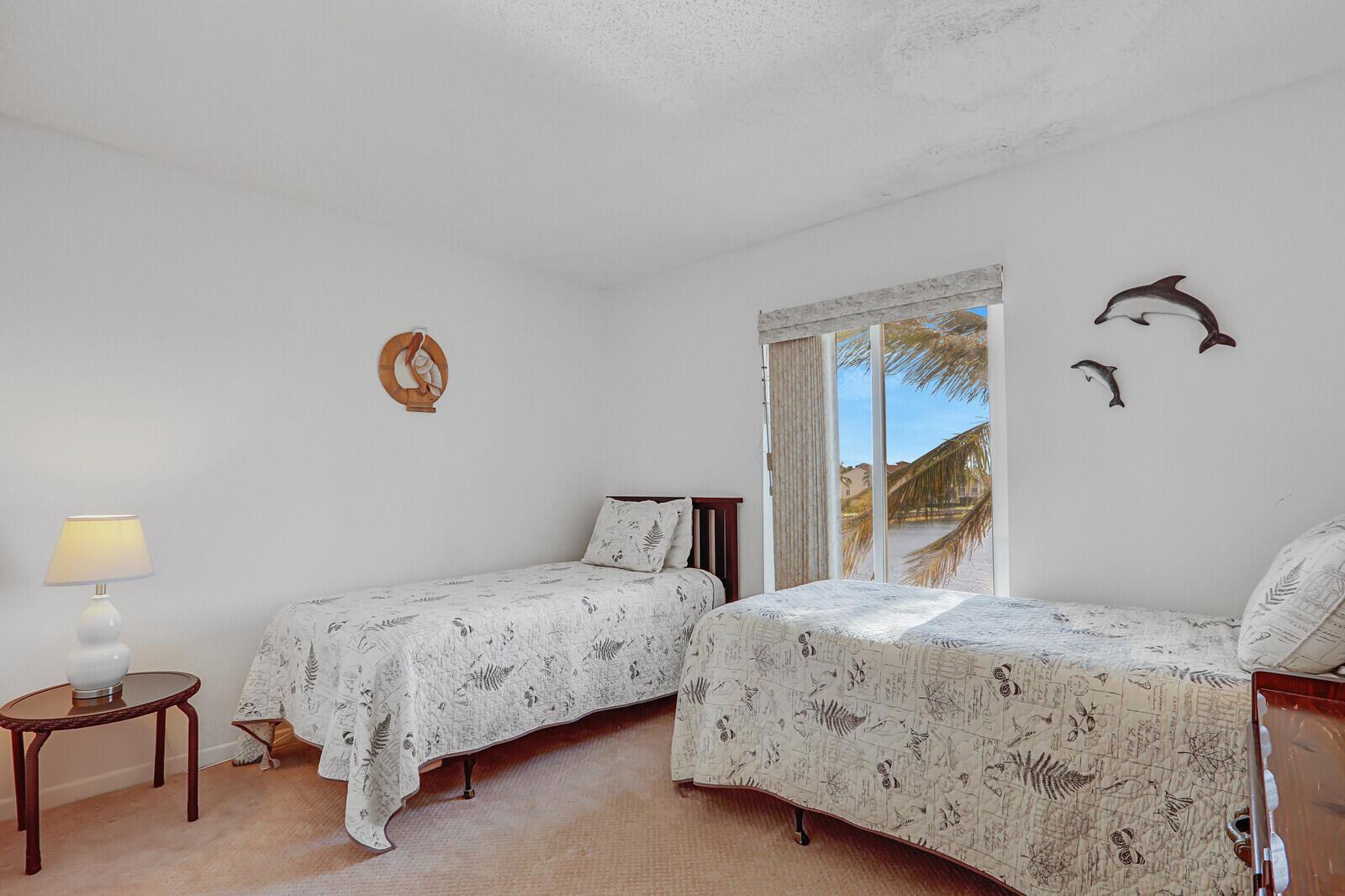 A bedroom with two twin beds, a side table with a lamp, and a window view — 4468 NE Ocean Boulevard # 3, Jensen Beach FL 34957, JENSEN BEACH, FL