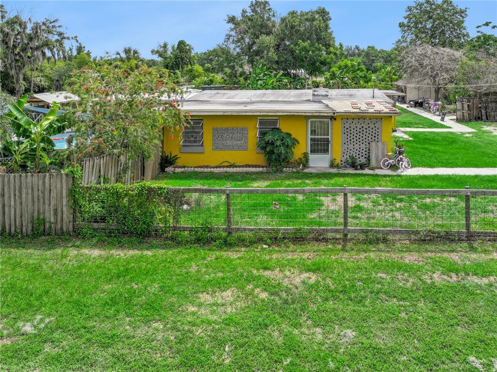 A yellow single-story house with a flat roof sits behind a wooden wire fence — 825 COOK ROAD, MULBERRY, FL