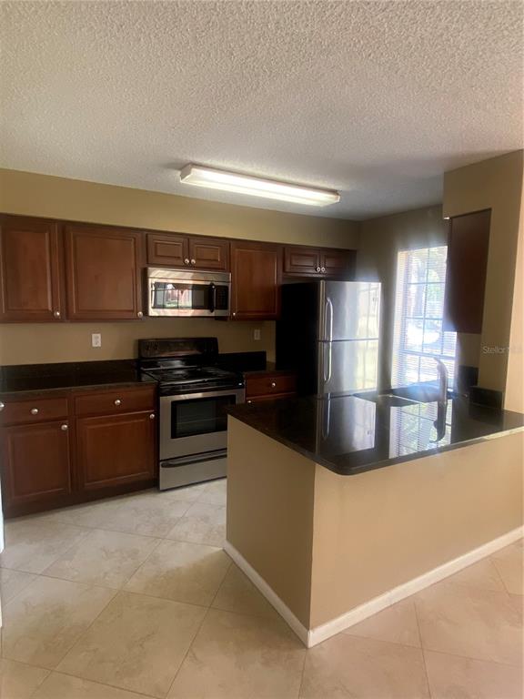 A kitchen features wood cabinets, stainless steel appliances, and a dark countertop island — 8724 MALLARD RESERVE DRIVE UNIT 102, TAMPA, FL