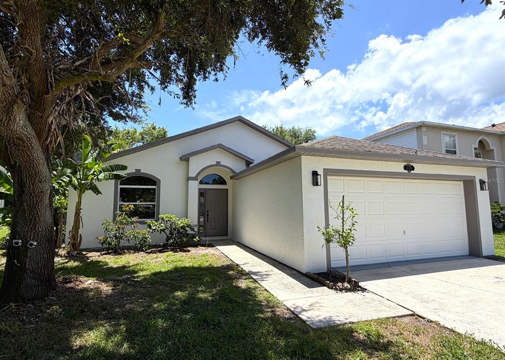 A single-story house with a white exterior, a two-car garage, and a large shade tree — 649 MACON DRIVE, TITUSVILLE, FL
