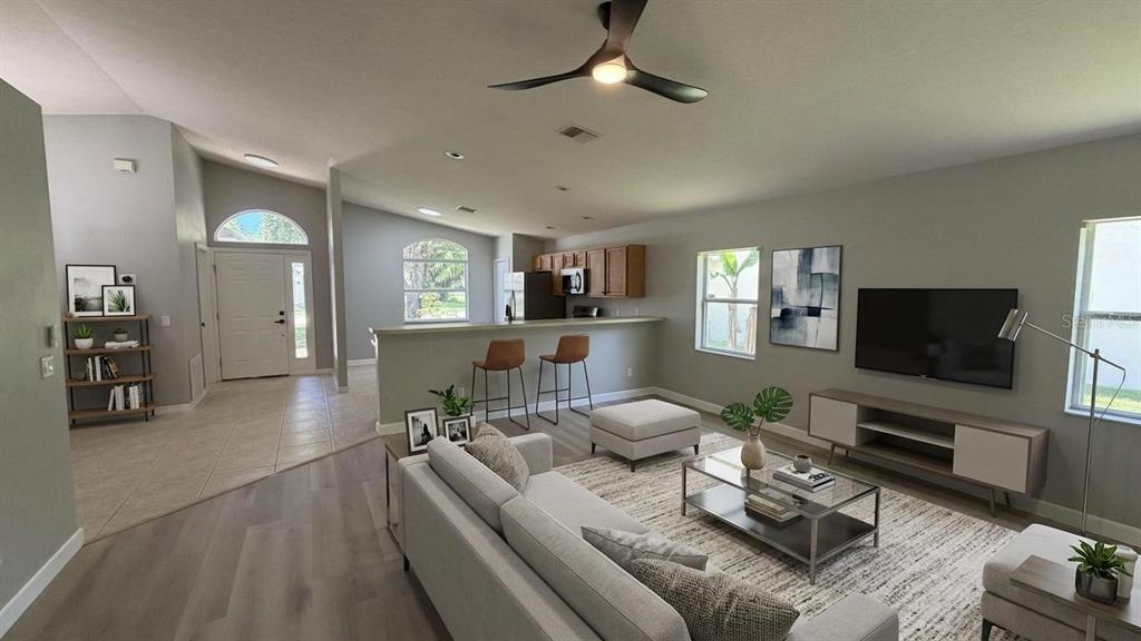 An open-concept living room and kitchen area features light wood flooring, neutral walls, and furniture — 649 MACON DRIVE, TITUSVILLE, FL