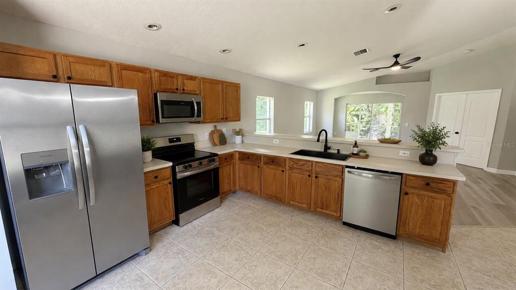 A kitchen features stainless steel appliances, wood cabinets, and a black sink on tile flooring — 649 MACON DRIVE, TITUSVILLE, FL
