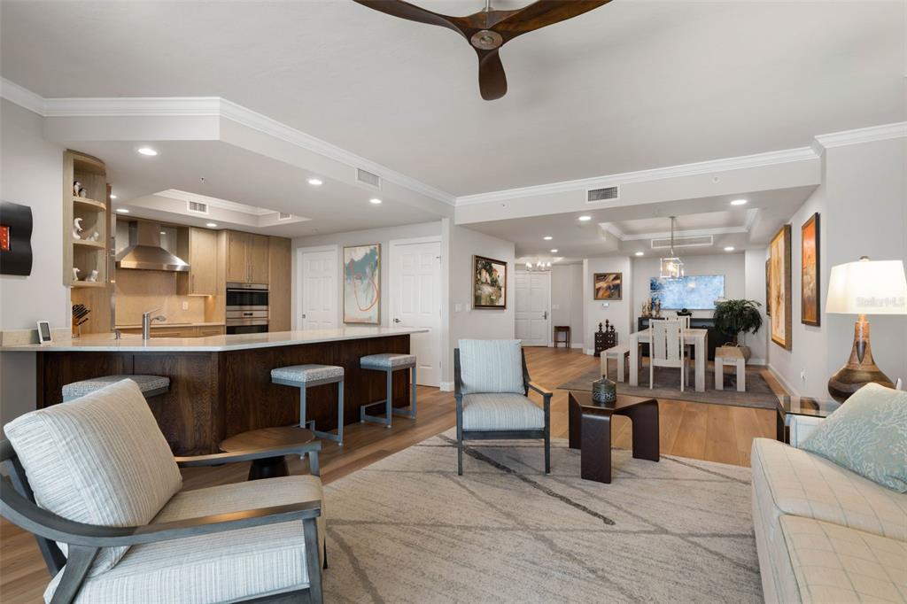 An open-concept living and dining area features a kitchen island, wood flooring, and neutral furniture — 19 AVENUE DE LA MER UNIT 502, PALM COAST, FL