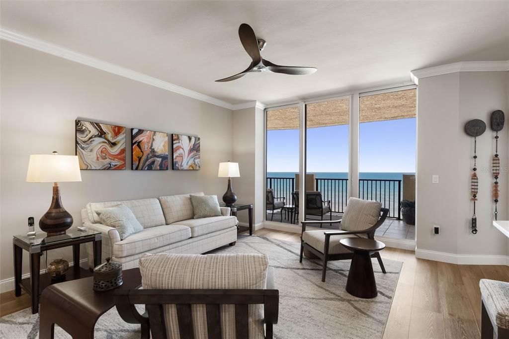 A living room features a sofa, armchairs, a ceiling fan, and a balcony overlooking the ocean — 19 AVENUE DE LA MER UNIT 502, PALM COAST, FL