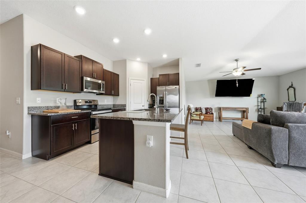 A kitchen with dark wood cabinets and granite countertops opens into a living room area — 16638 DELIA STREET, WIMAUMA, FL