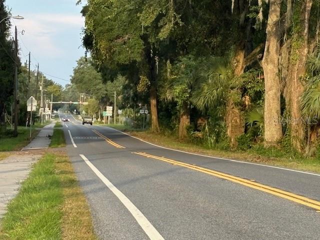 A paved road stretches forward lined by trees and utility poles under a clear sky — SW 4TH AVE., CHIEFLAND, FL