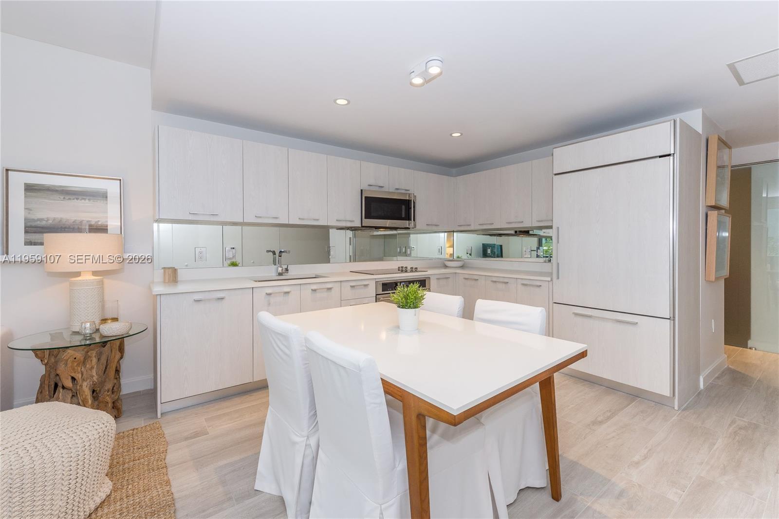 A modern kitchen features light wood cabinetry, a mirrored backsplash, and a white dining set — 55 SW 9th St # 1010, Miami FL 33130, MIAMI, FL