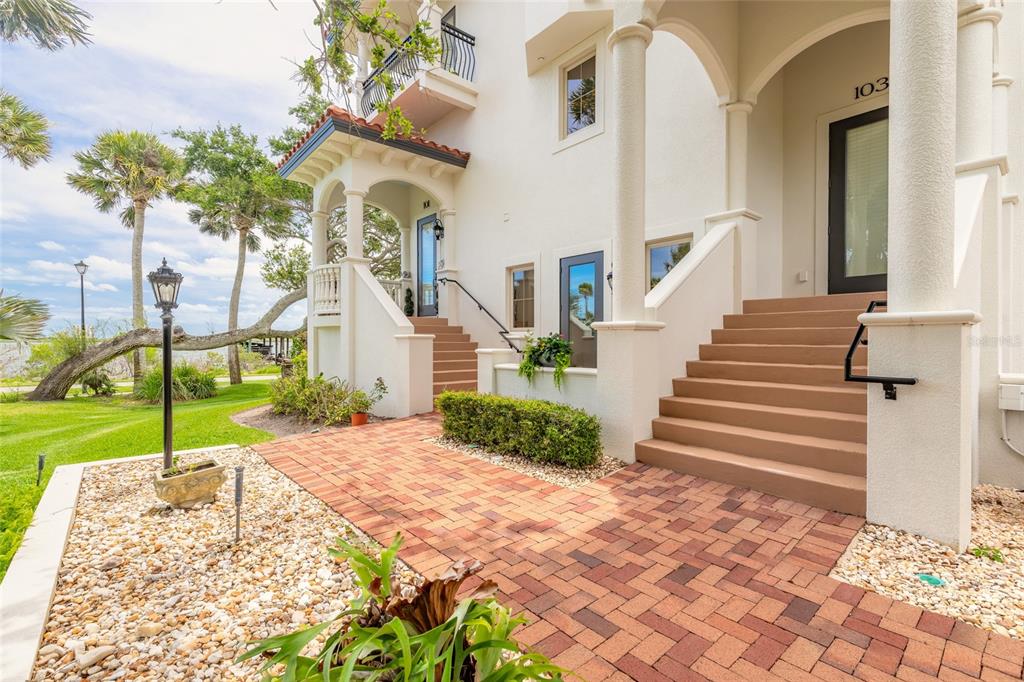An exterior view of a white multi-story building with brick stairs and a paved walkway — 5090 RIVERSIDE DRIVE UNIT 103, PORT ORANGE, FL