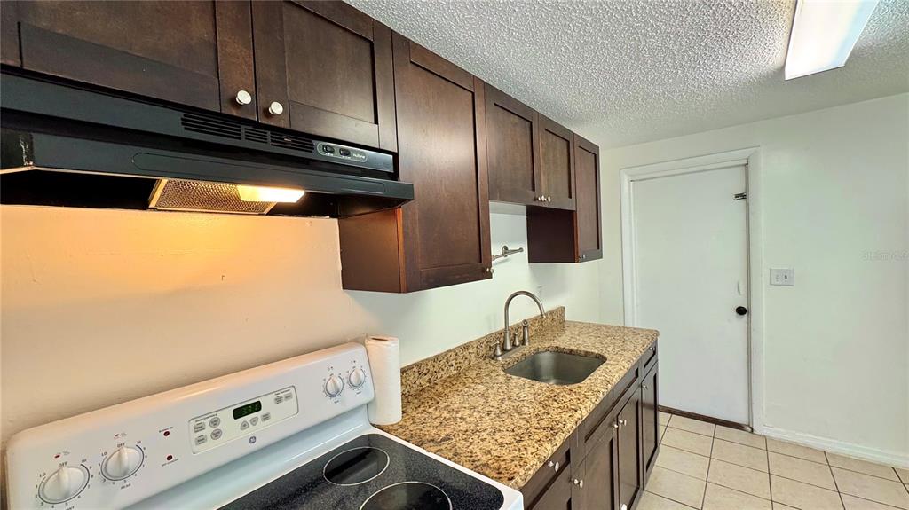 A kitchen features dark wood cabinets, a granite countertop, a stainless sink, and a stove — 3780 137TH AVENUE, LARGO, FL