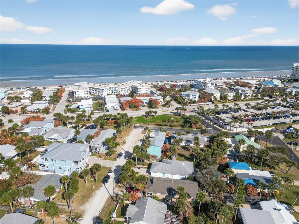 An aerial view shows a coastal neighborhood with houses, palm trees, and a sandy beach — 923 LOCUST STREET, NEW SMYRNA BEACH, FL