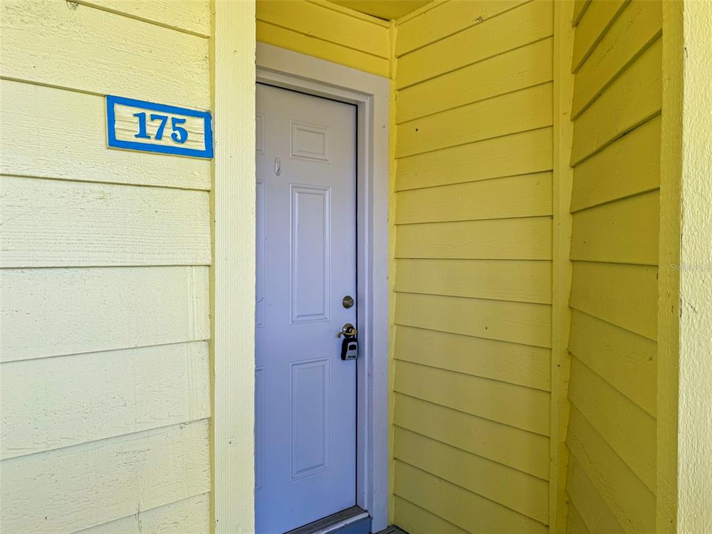 A yellow exterior wall features a white door marked with the number 175 — 455 ALT 19 S UNIT 175, PALM HARBOR, FL