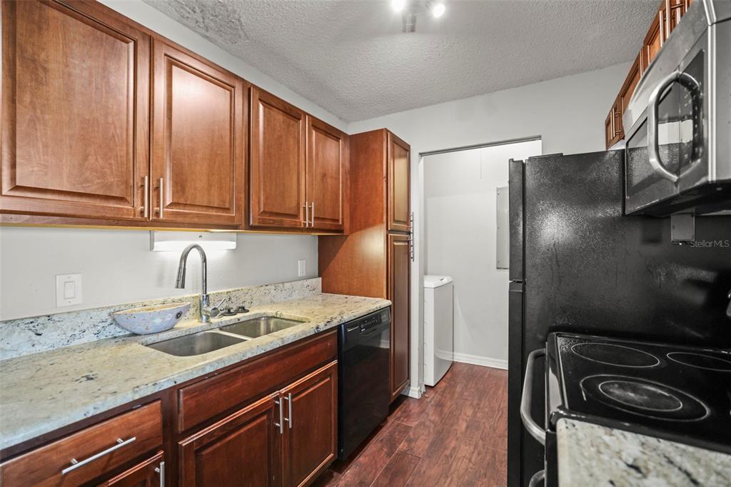 A kitchen with wood cabinets, granite countertops, black appliances, and a view into a laundry area — 455 ALT 19 S UNIT 175, PALM HARBOR, FL