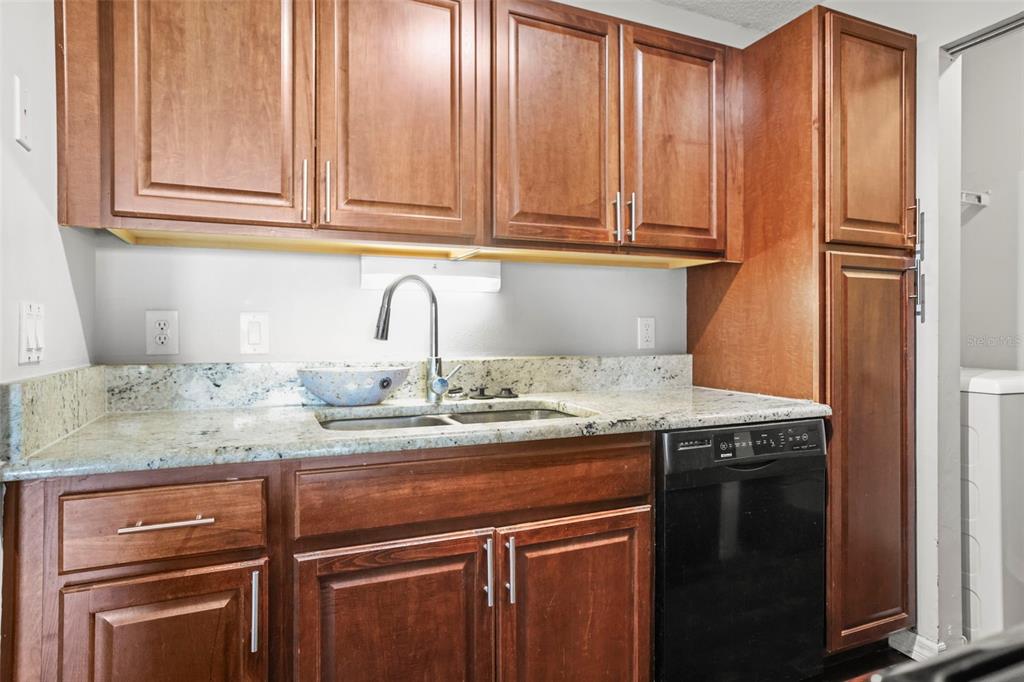 A kitchen features wood cabinets, granite countertops, a stainless steel faucet, and a black dishwasher — 455 ALT 19 S UNIT 175, PALM HARBOR, FL