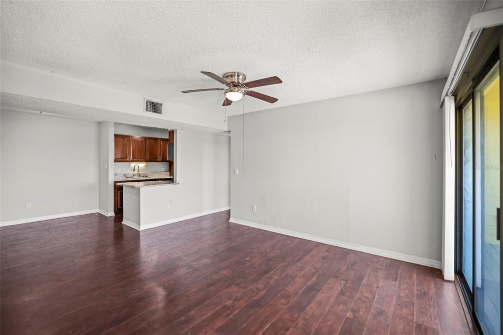 A living room with dark wood flooring, a ceiling fan, and an open kitchen area — 455 ALT 19 S UNIT 175, PALM HARBOR, FL