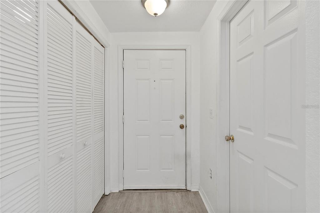 A white entryway features a front door, louvered closet doors, and light-colored wood-look flooring — 3428 SOHO STREET UNIT B08, ORLANDO, FL