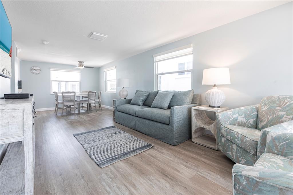 A living room with light blue walls, wood-look flooring, a blue sofa, and a dining area — 6020 MIDNIGHT PASS ROAD UNIT 53, SARASOTA, FL