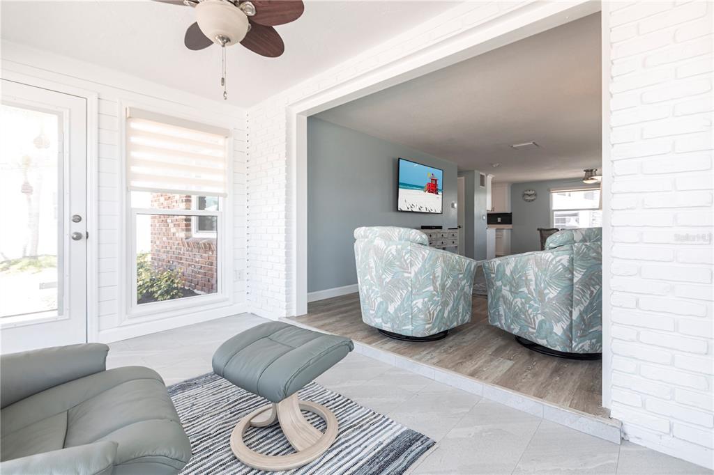 A sunroom with tile flooring leads into a living area with wood-look floors and chairs — 6020 MIDNIGHT PASS ROAD UNIT 53, SARASOTA, FL