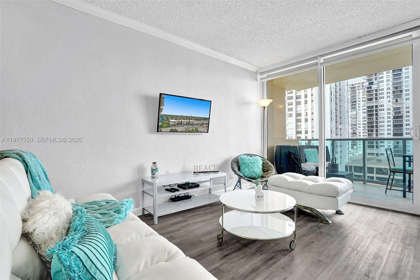 A bright living room features white furniture, a television, and a balcony with city views — 2501 S Ocean Dr, Hollywood FL 33019, HOLLYWOOD, FL
