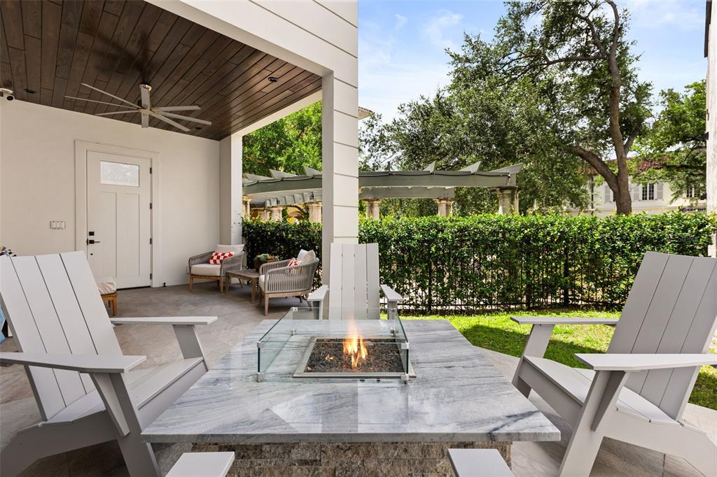A covered patio features a stone fire pit table, Adirondack chairs, and a wood-paneled ceiling — 660 W MORSE BOULEVARD, WINTER PARK, FL