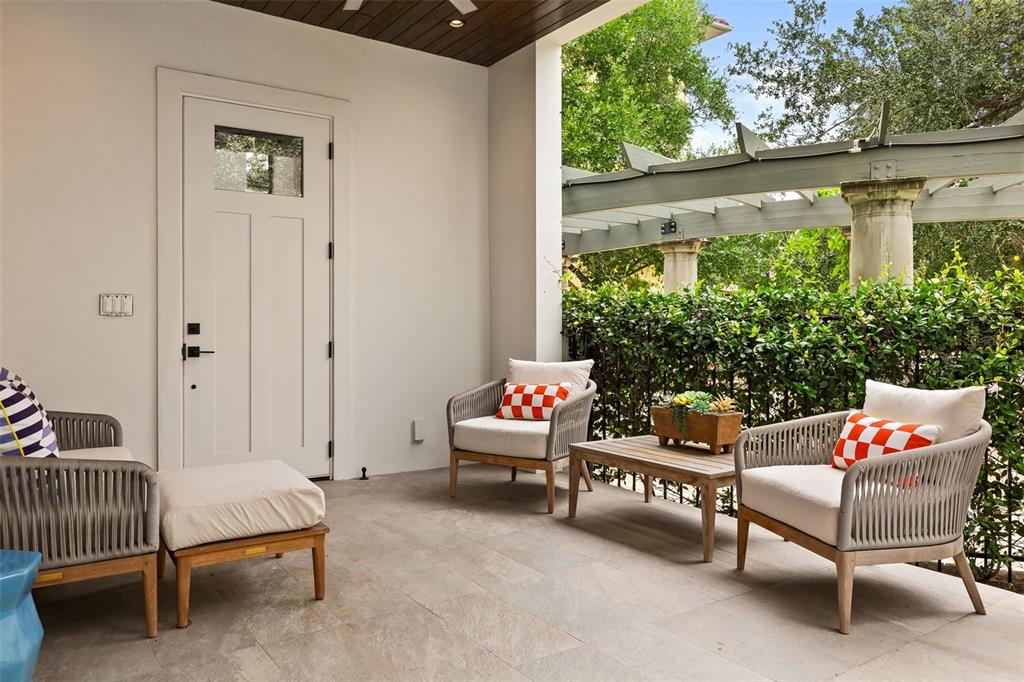 A covered patio features stone flooring, three armchairs with cushions, a coffee table, and a door — 660 W MORSE BOULEVARD, WINTER PARK, FL
