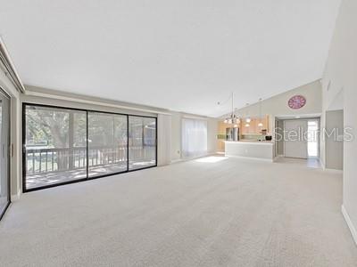 A spacious living room with beige carpeting, vaulted ceilings, and large sliding glass doors — 700 STARKEY ROAD UNIT 422, LARGO, FL