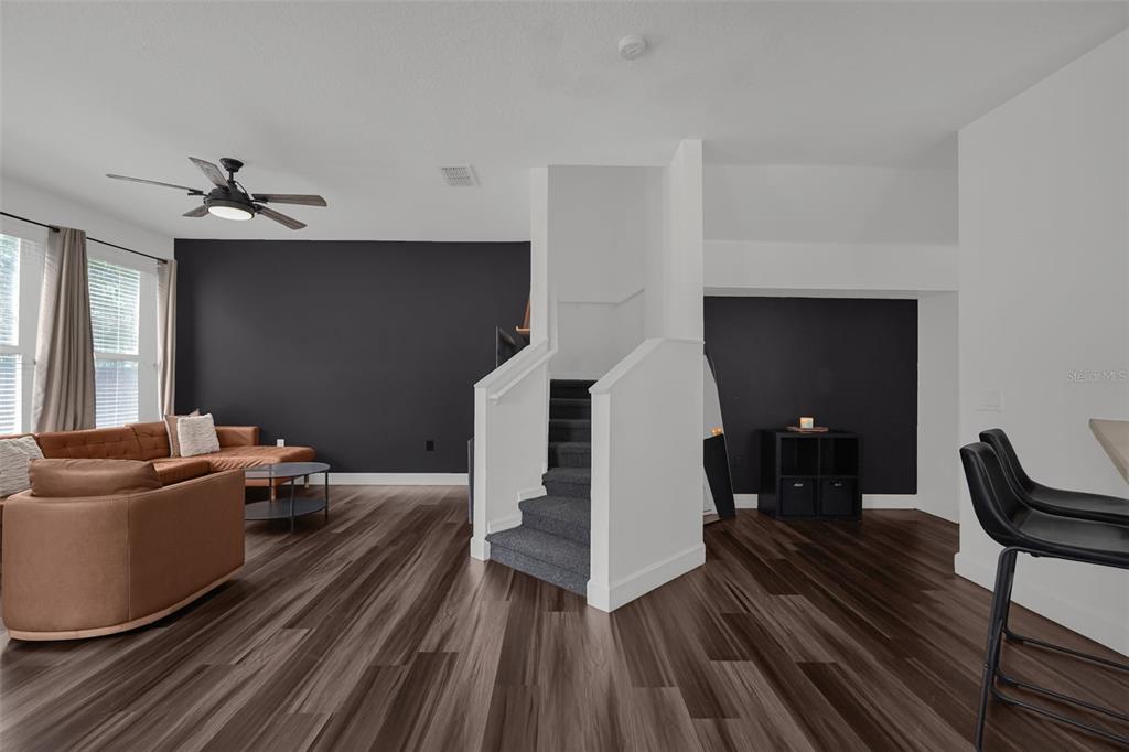 A living room features dark wood-look flooring, a charcoal accent wall, and a central staircase — 1933 ESTANCIA CIRCLE UNIT 1933, KISSIMMEE, FL
