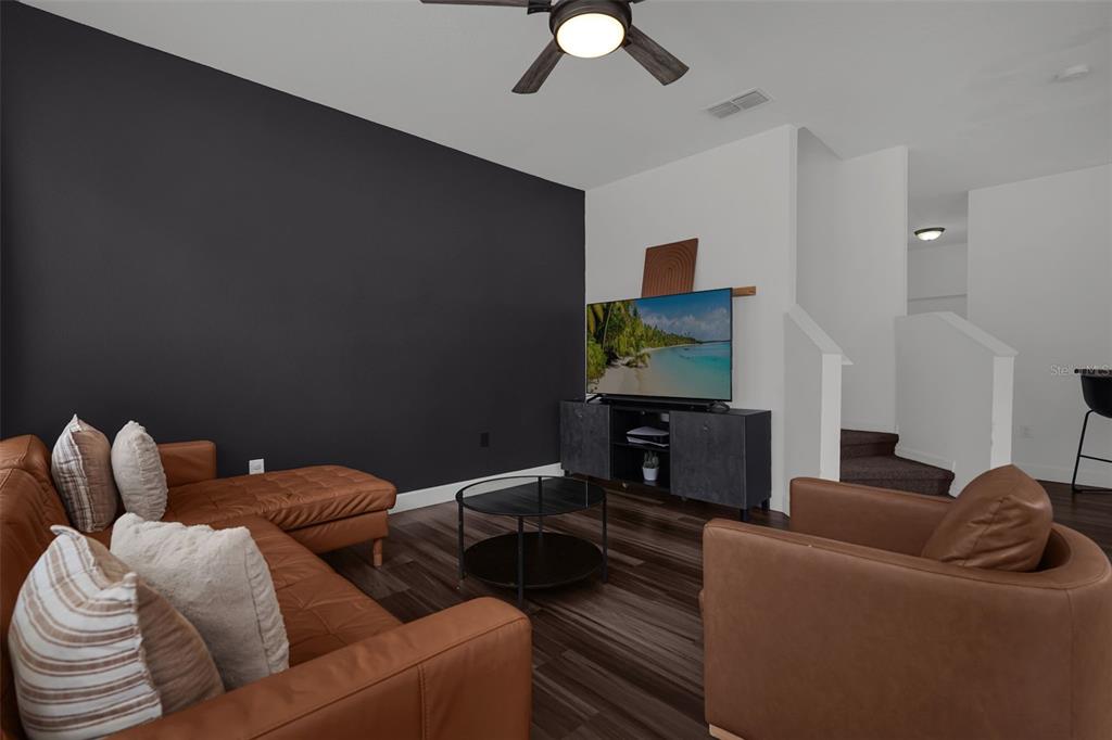 A living room features a dark accent wall, brown leather furniture, and a television console — 1933 ESTANCIA CIRCLE UNIT 1933, KISSIMMEE, FL