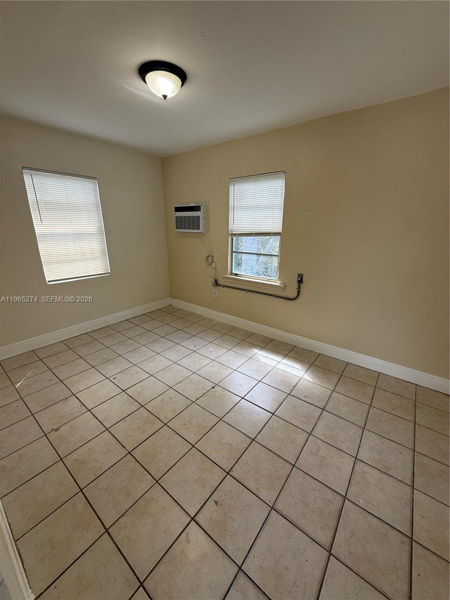 An empty room features beige walls, tiled flooring, two windows with blinds, and an air conditioner — 8290 NW 4th Ave # 2, Miami FL 33150, MIAMI, FL