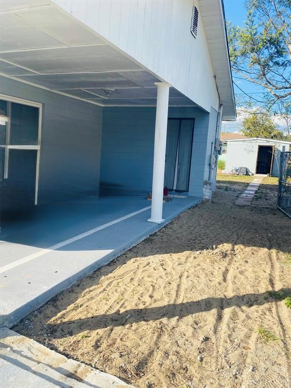 A covered concrete patio with a white column sits beside a sandy yard and shed — 2337 LAURA STREET, LAKE WALES, FL