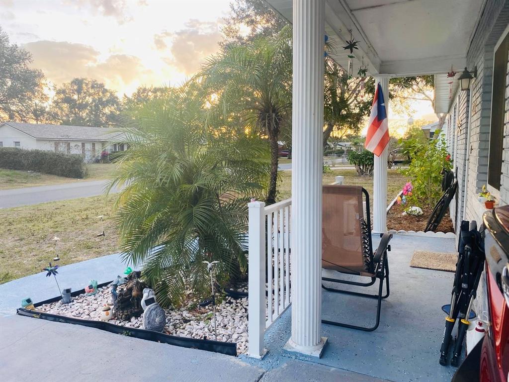 A covered front porch features a palm tree, a chair, and a hanging Puerto Rican flag — 2337 LAURA STREET, LAKE WALES, FL
