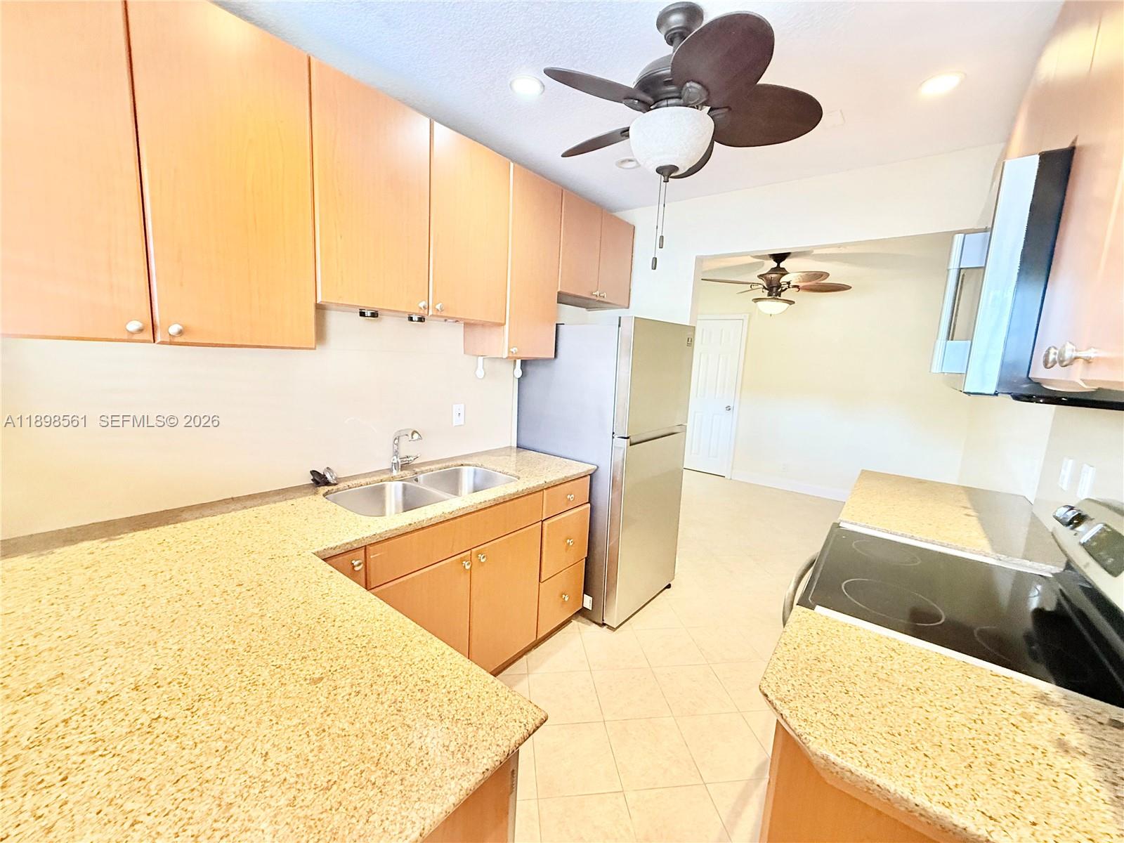 A kitchen features light wood cabinets, granite countertops, stainless steel appliances, and a ceiling fan — 3600 Harrison St # 16B, Hollywood FL 33021, HOLLYWOOD, FL