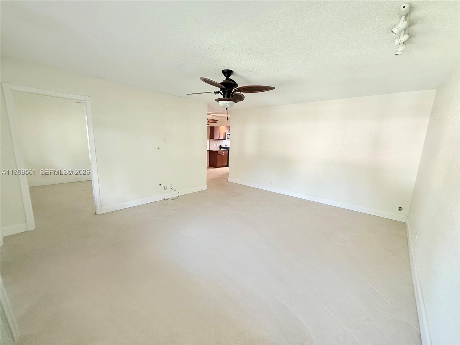 A living room with beige carpet, white walls, a ceiling fan, and a kitchen view — 3600 Harrison St # 16B, Hollywood FL 33021, HOLLYWOOD, FL