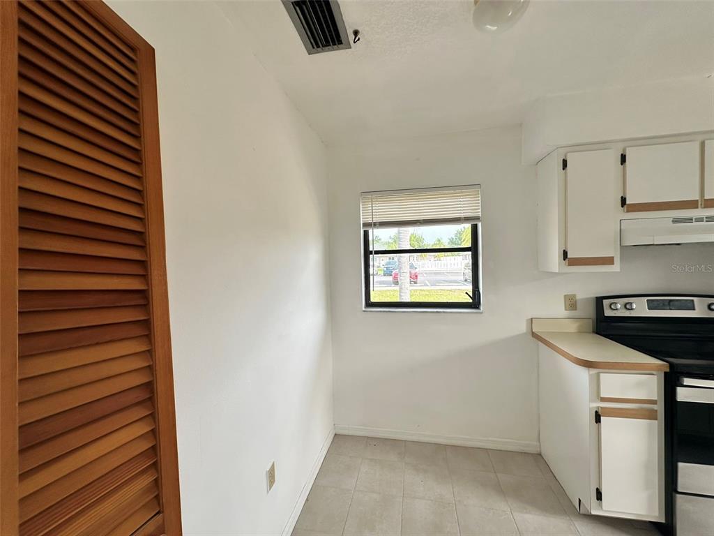 A kitchen features white cabinets, a black stove, tiled flooring, and a window with blinds — 24540 HARBORVIEW ROAD UNIT F2, PORT CHARLOTTE, FL