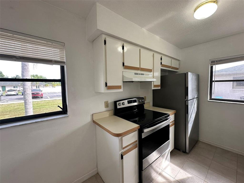 A kitchen features white cabinets, laminate countertops, a black stove, and a stainless steel refrigerator — 24540 HARBORVIEW ROAD UNIT F2, PORT CHARLOTTE, FL