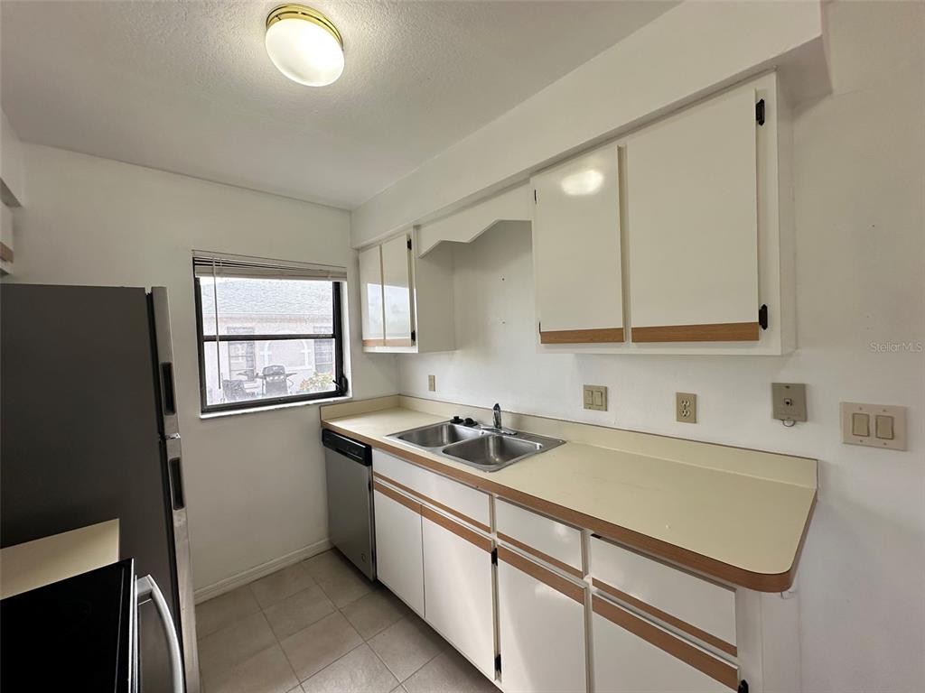 A kitchen features white cabinets, a laminate countertop, a stainless steel sink, and a window — 24540 HARBORVIEW ROAD UNIT F2, PORT CHARLOTTE, FL