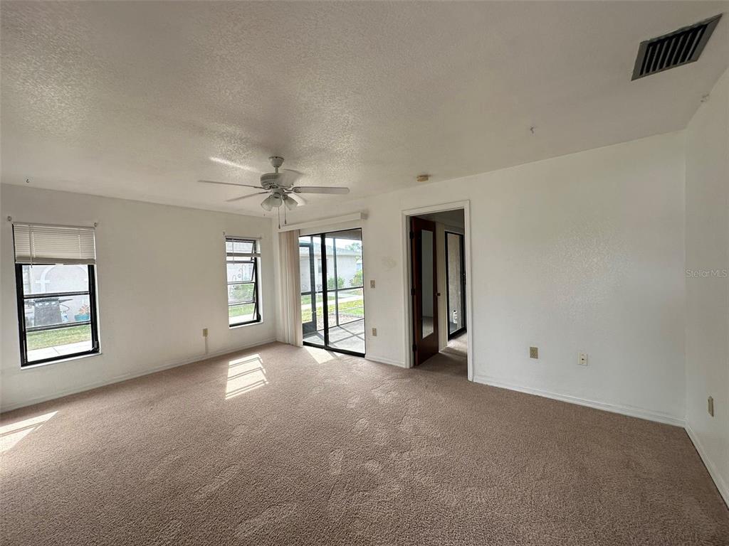 A carpeted living room features a ceiling fan, sliding glass doors, and a doorway — 24540 HARBORVIEW ROAD UNIT F2, PORT CHARLOTTE, FL