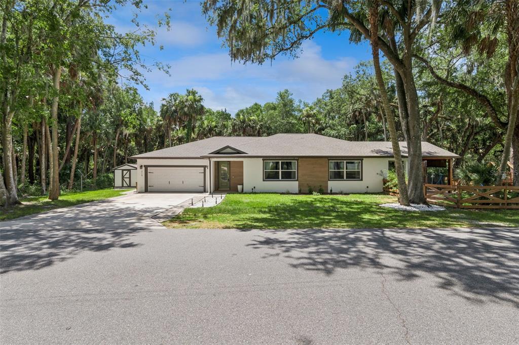 A single-story house with a white and wood-paneled exterior, a two-car garage, and surrounding trees — 215 SUNRISE BOULEVARD, DEBARY, FL
