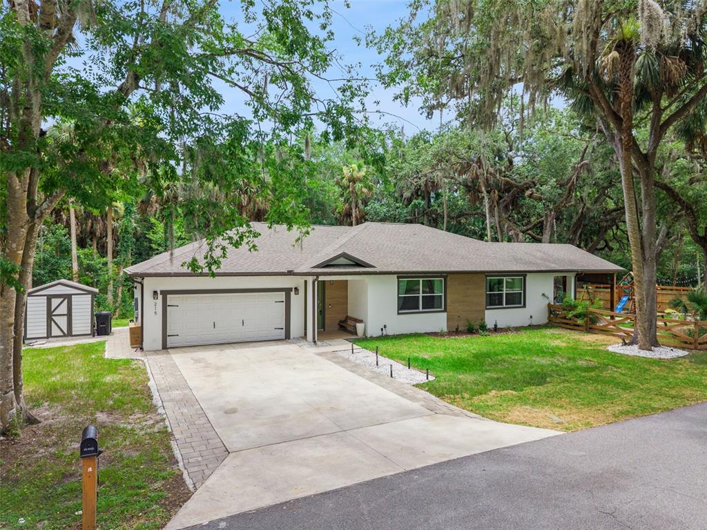 A single-story house with a white exterior, wood-look siding, and a concrete driveway — 215 SUNRISE BOULEVARD, DEBARY, FL