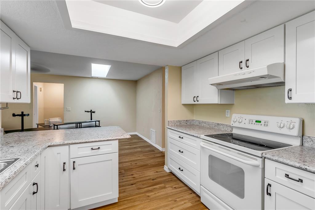 A kitchen features white cabinets, granite countertops, a white range, and wood-look flooring — 704 GREEN ROAD, NEW SMYRNA BEACH, FL